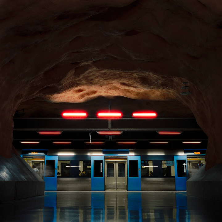 A subway train with open doors is stopped at a station with a rough, cave-like ceiling illuminated by red lights.
