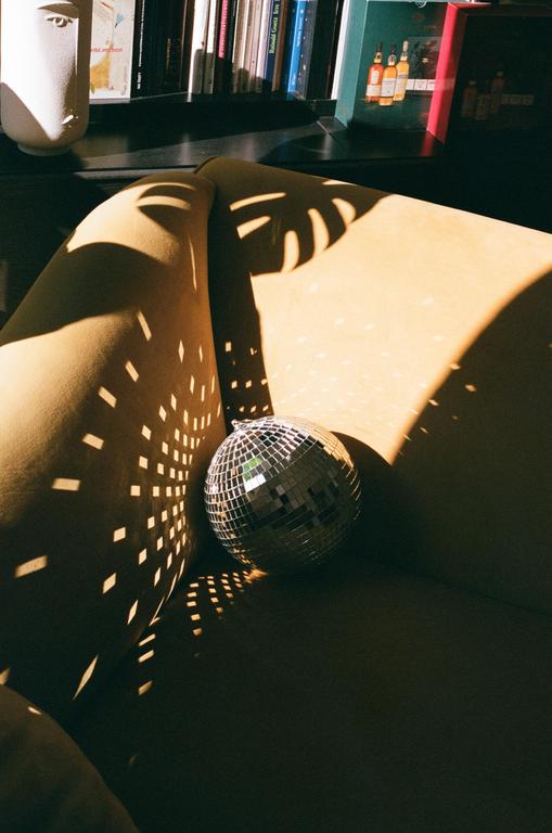 A disco ball rests on a person's lap, reflecting light patterns onto their legs and the surrounding surface.
