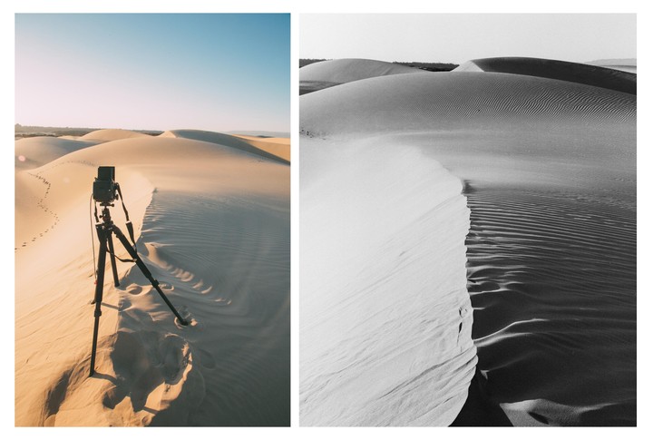 A camera on a tripod stands on a sand dune next to a black and white image of sand dunes.