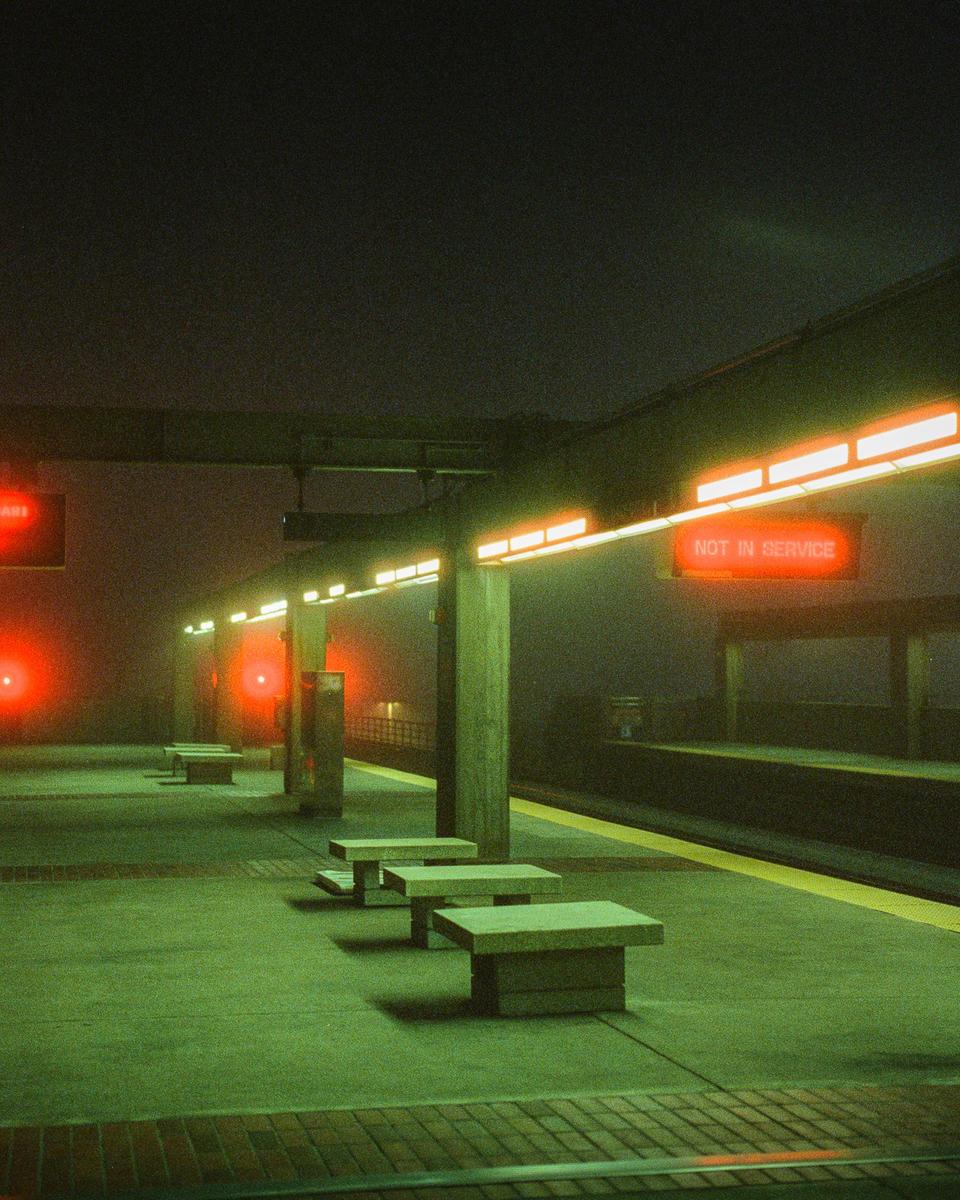 A train platform with benches and a "not in service" sign is illuminated by red and orange lights at night.