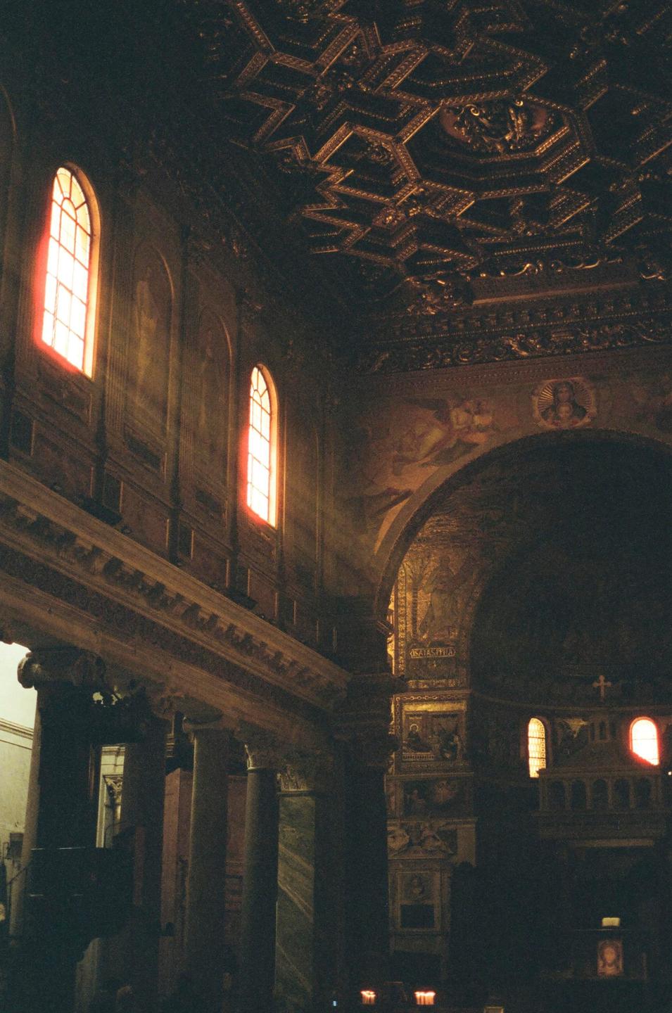 Sunlight streams through arched windows into a grand, ornate interior with a coffered ceiling.