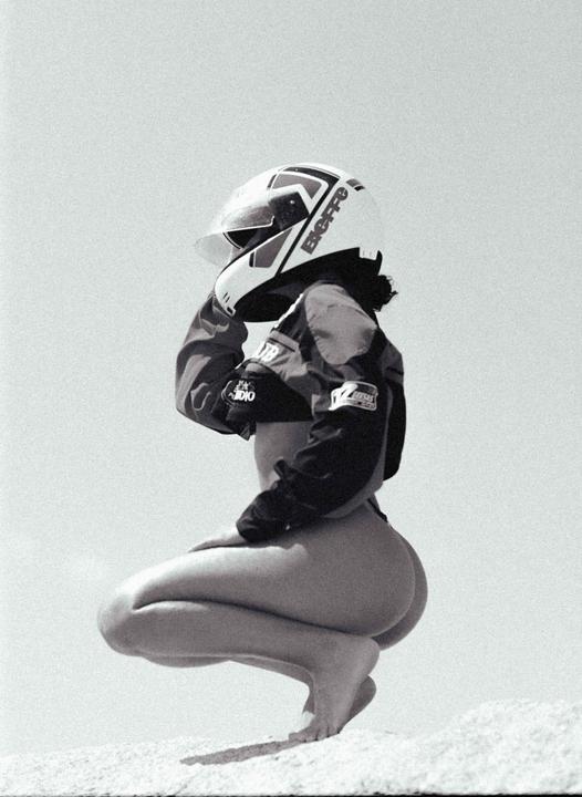 A woman wearing a helmet and jacket crouches on a light-colored surface.