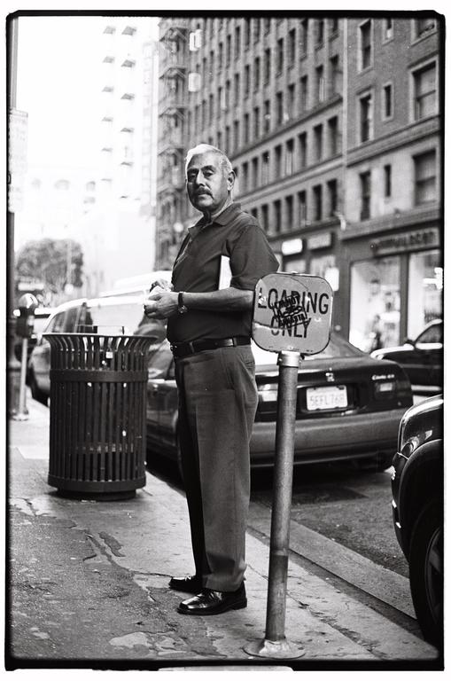 A man stands on a city sidewalk next to a trash can and a "loading only" sign.