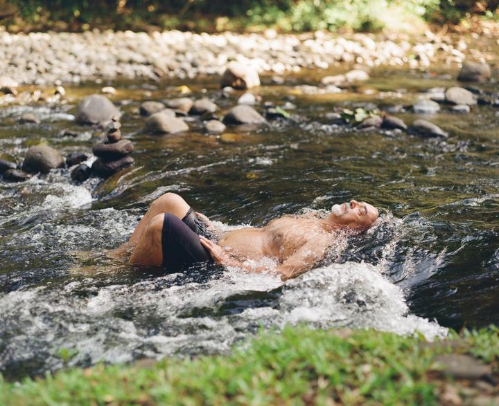 A man with a white beard is floating on his back in a rocky river.