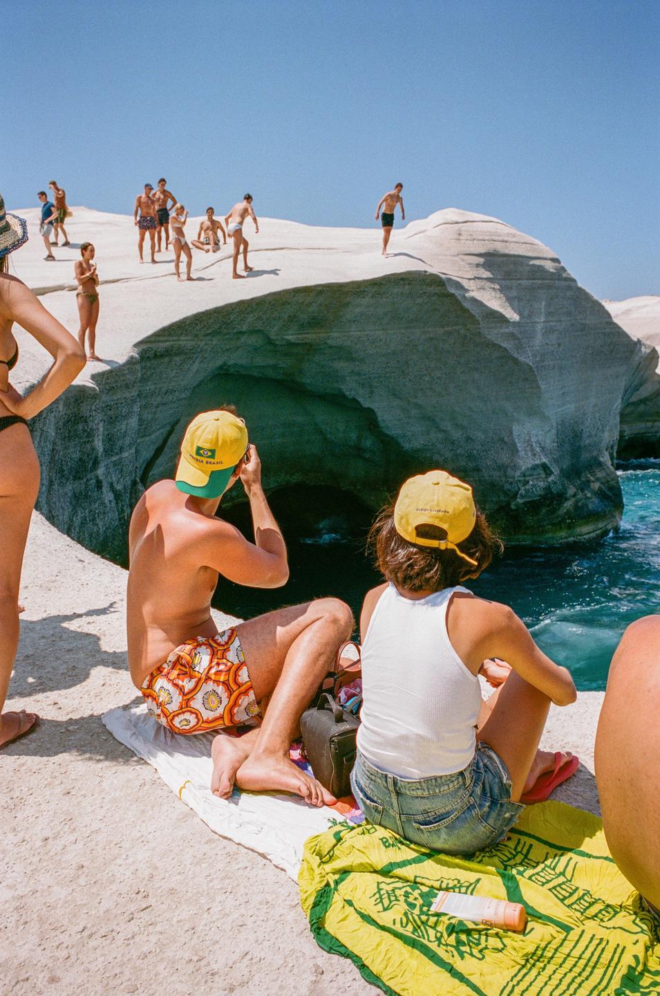 A group of people are relaxing on a white rock formation next to the ocean under a clear blue sky.