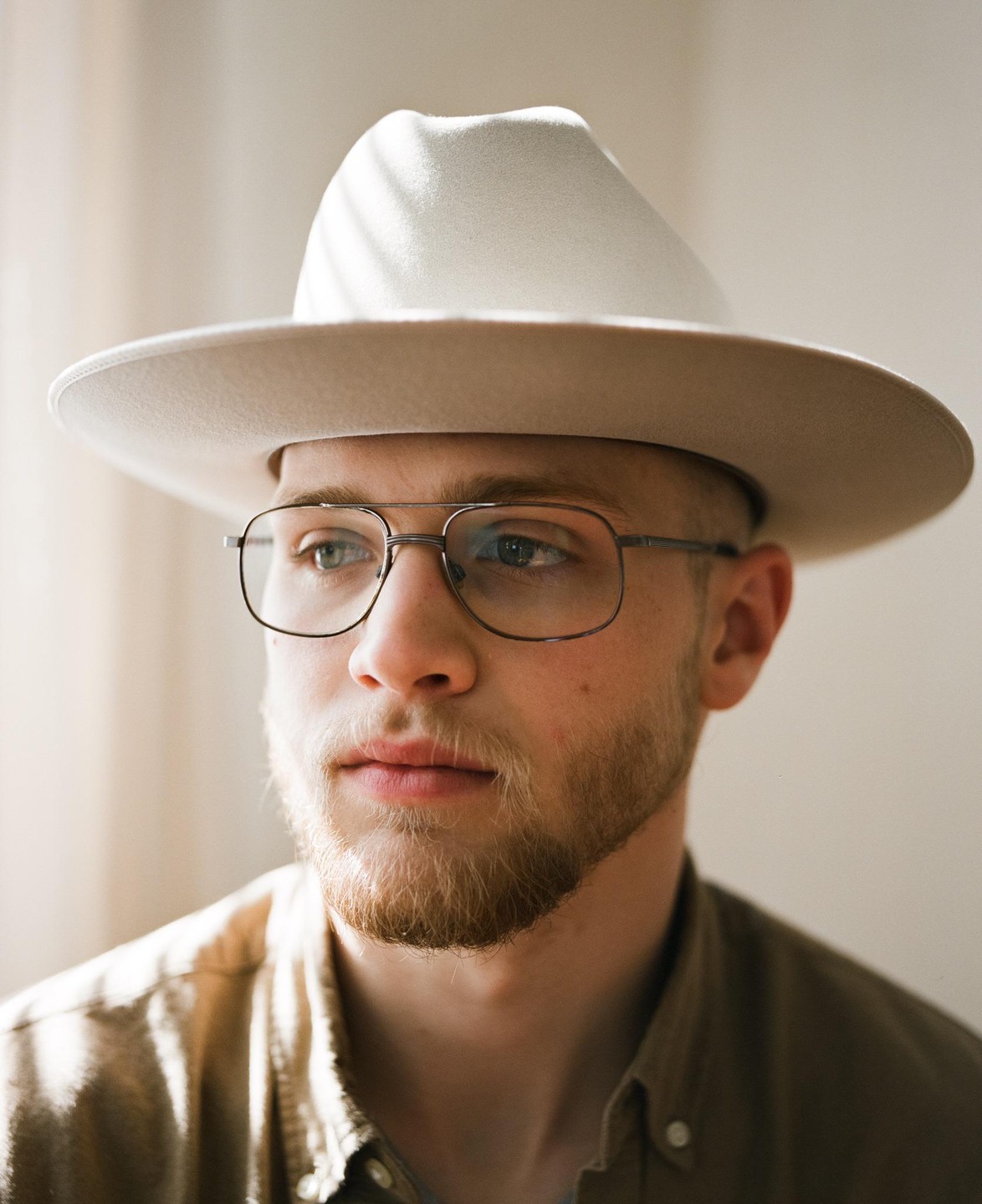 A man wearing a hat and glasses looks to the side, with shadows cast across his hat.