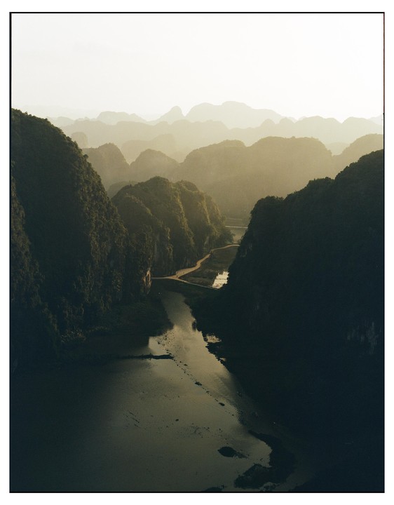 A river winds through a valley surrounded by lush, green mountains under a hazy sky.