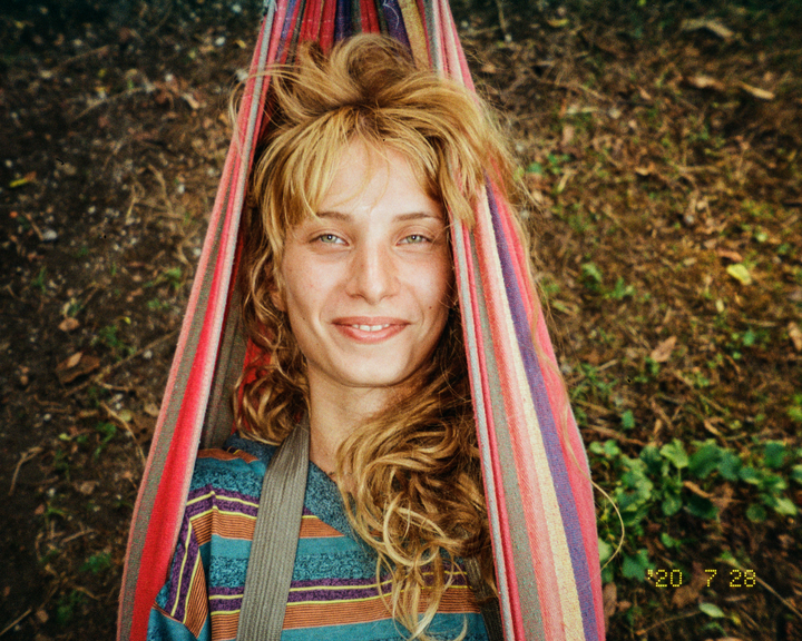 A woman with long, curly hair smiles while lying in a colorful striped hammock.