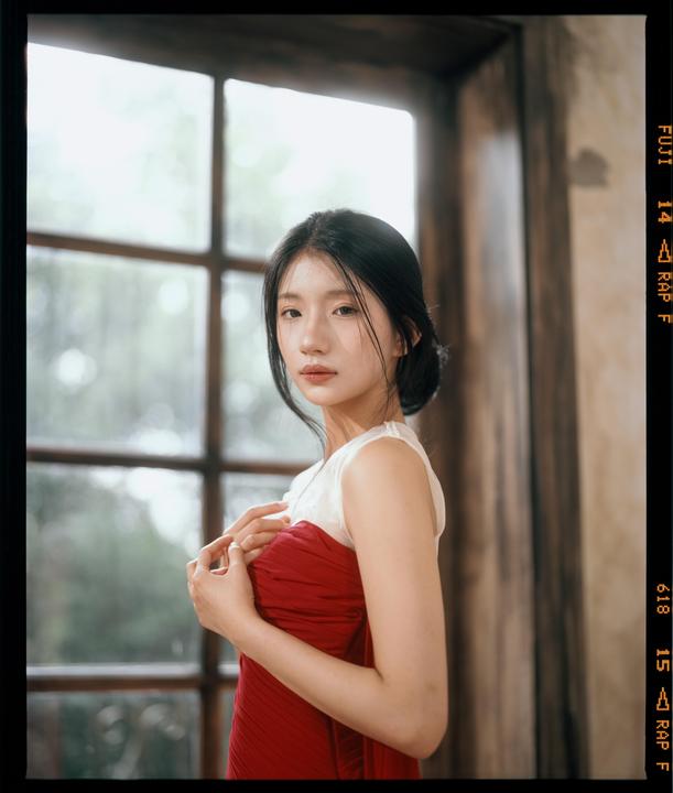 A woman in a red dress stands in front of a window.