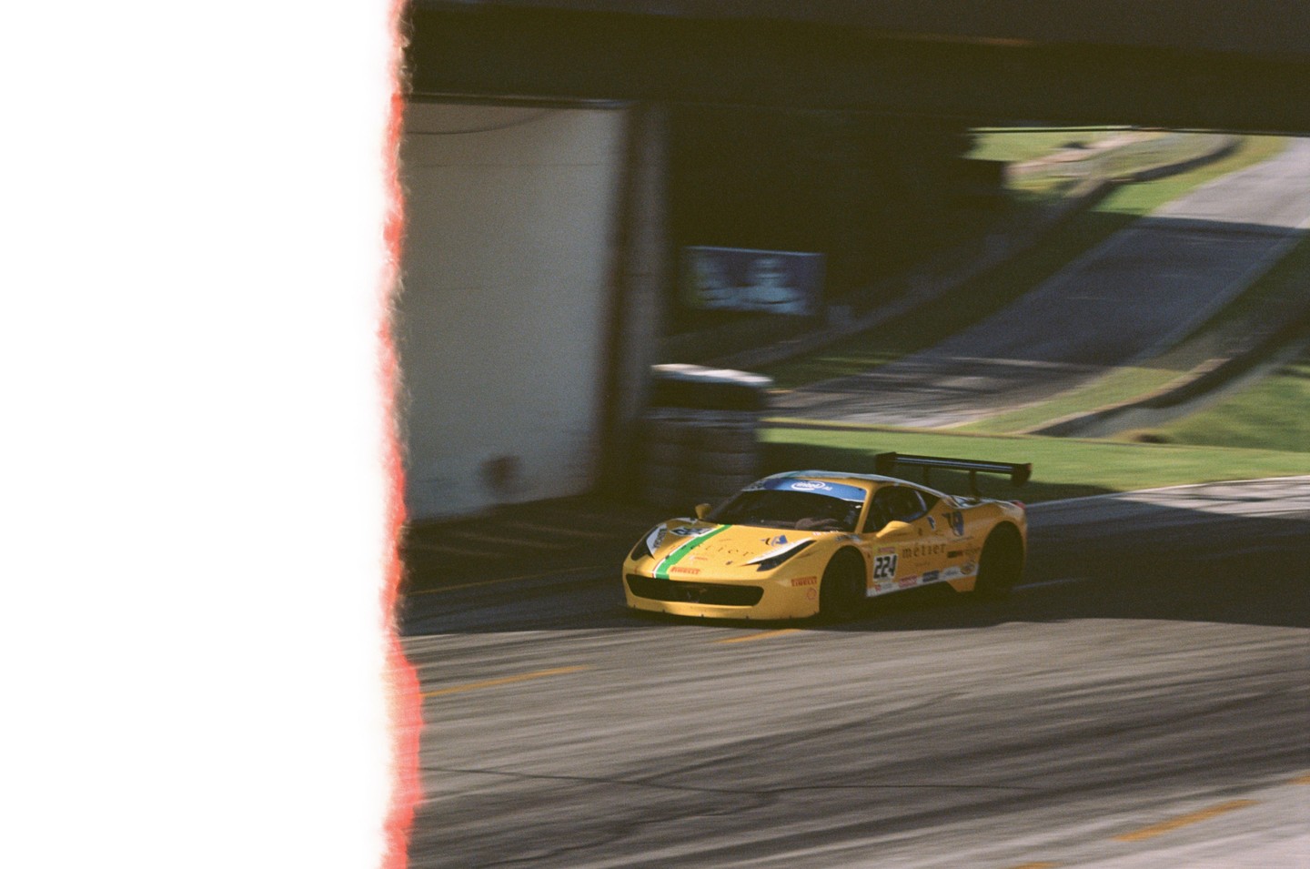 A yellow race car with green stripes speeds along a track with a blurred background.