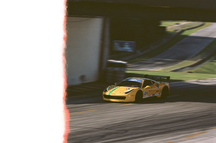 A yellow race car with green stripes speeds along a track with a blurred background.