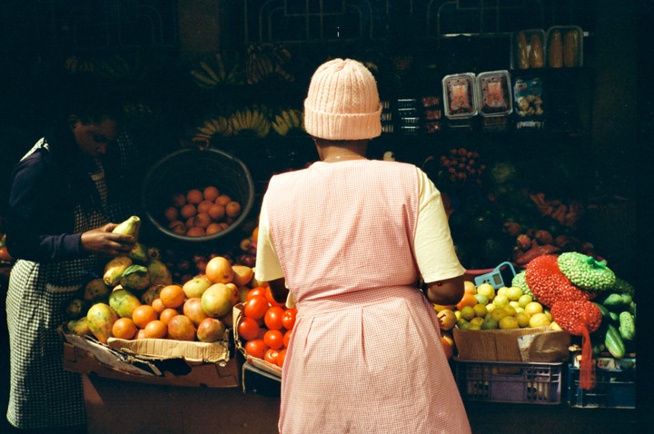 Two women are selling fruit and vegetables at a market stall.