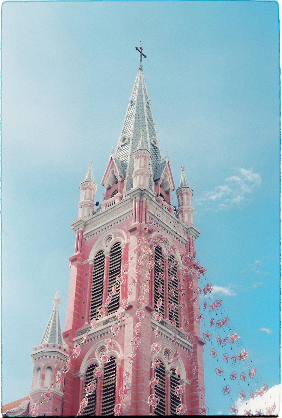 A pink church tower with a cross on top is adorned with star-shaped decorations against a blue sky.