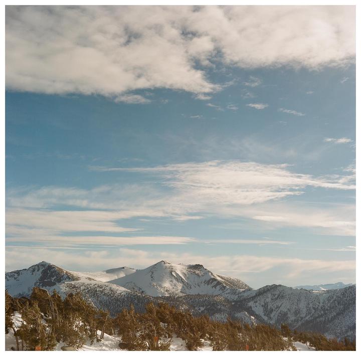 Snow-covered mountains and trees are visible under a blue sky with clouds.