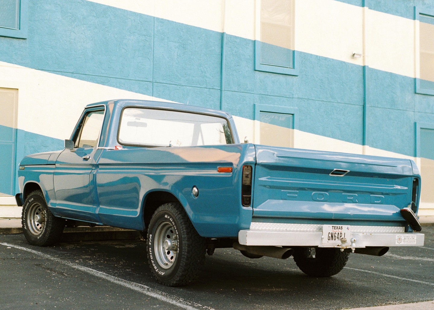 A turquoise pickup truck is parked in front of a building with turquoise and white stripes.
