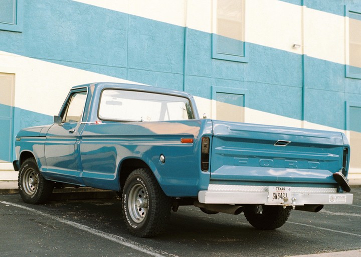 A turquoise pickup truck is parked in front of a building with turquoise and white stripes.