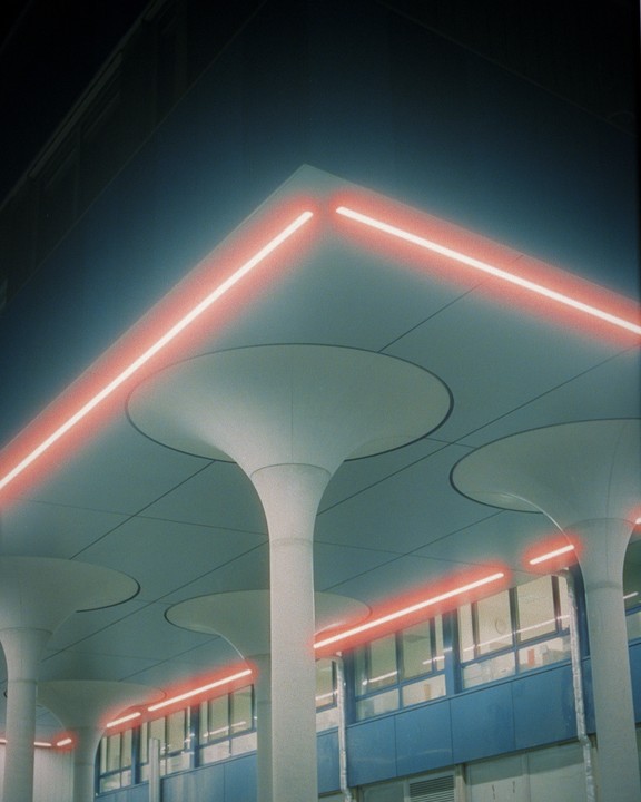 Red neon lights illuminate the ceiling and pillars of a modern building at night.