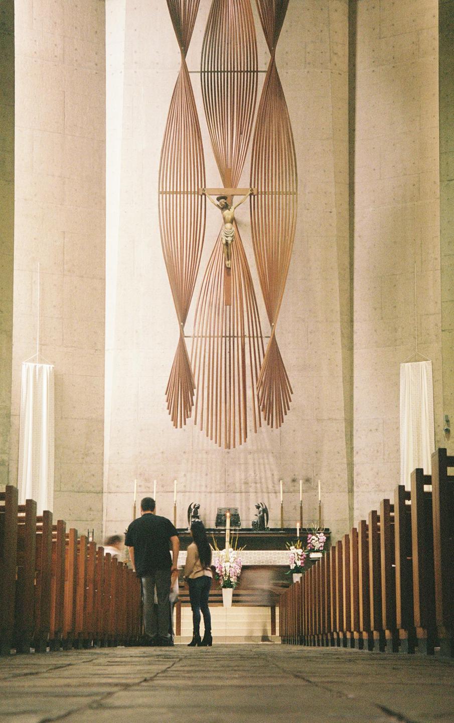 A couple stands in a church aisle looking towards an altar with a crucifix hanging above it.