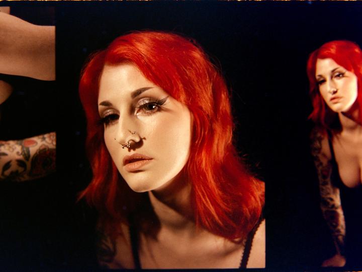 A woman with red hair and a nose piercing is shown in a studio portrait, with a second, blurry image of her visible to the right.