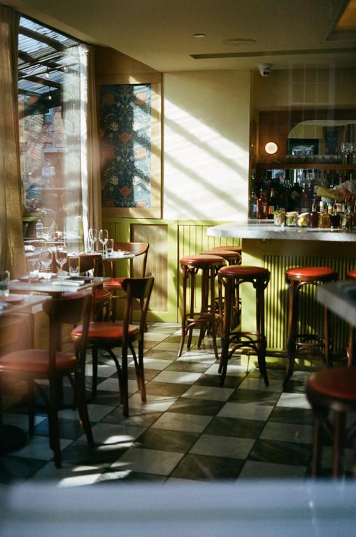 Sunlight streams into a restaurant with checkered floors, tables, and a bar with stools.