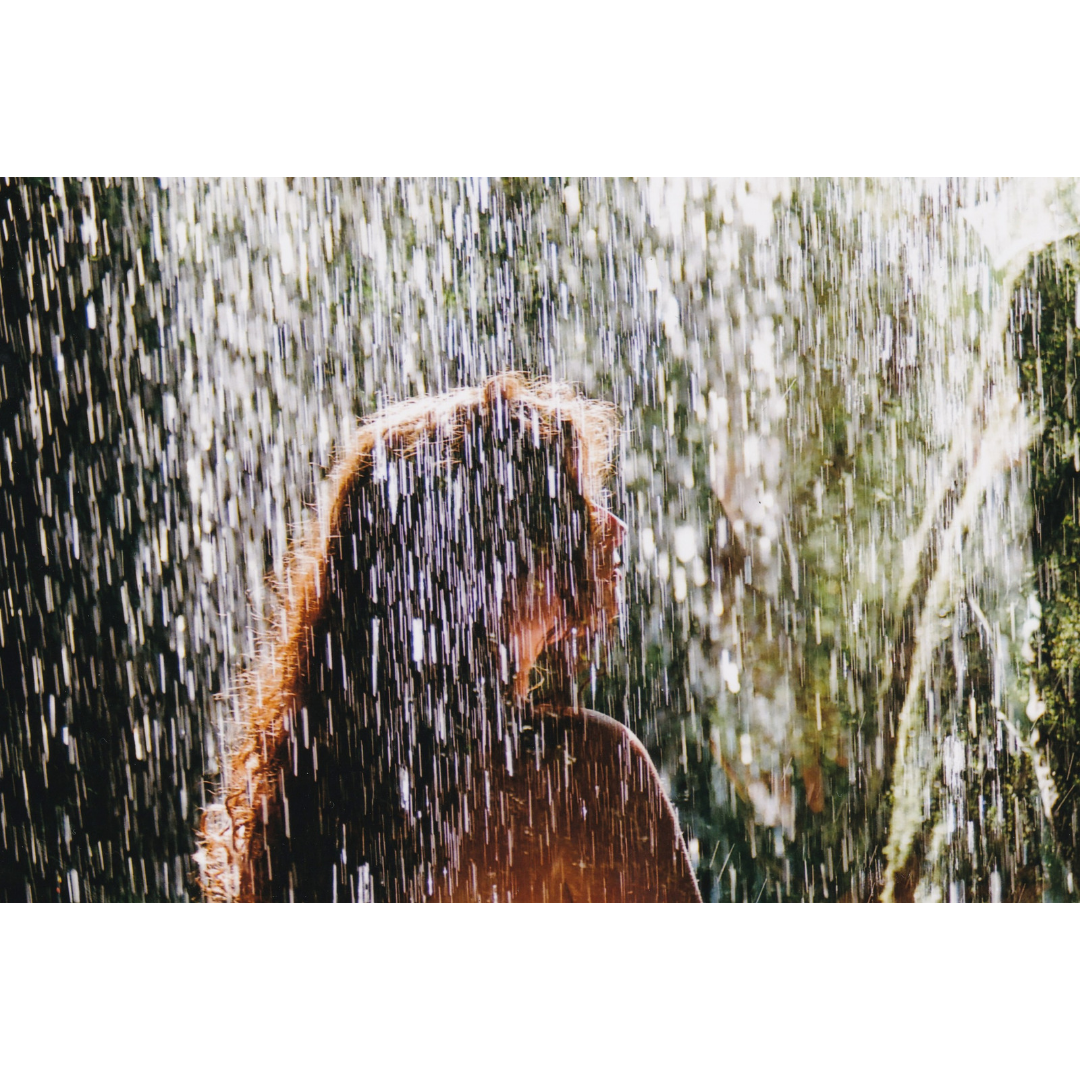 A woman with long, curly hair stands in the rain, looking to the right.