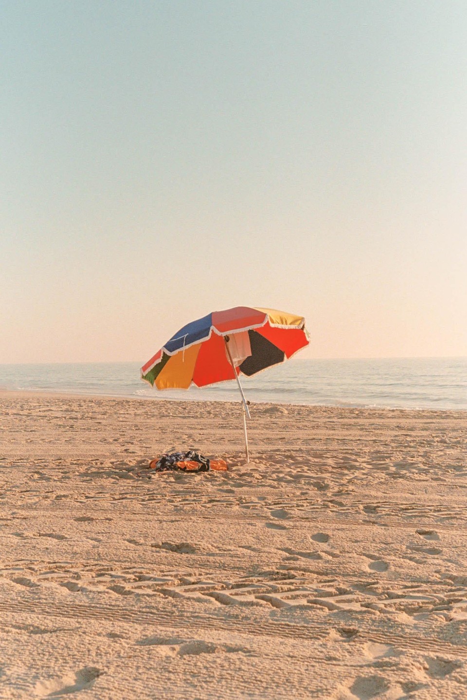 A colorful beach umbrella stands on a sandy beach next to the ocean.