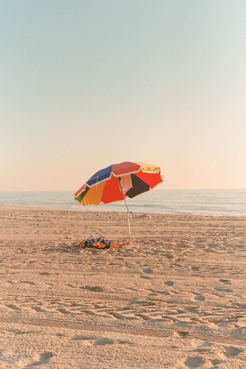 A colorful beach umbrella stands on a sandy beach next to the ocean.