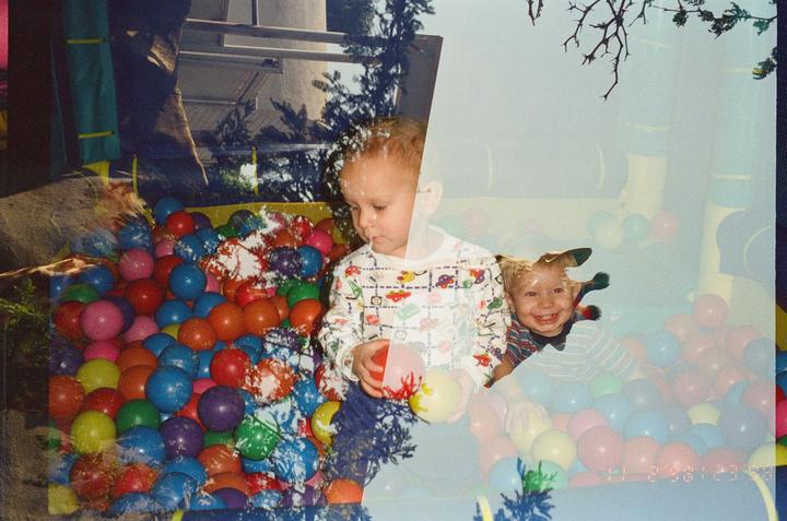 Two children play in a ball pit in a double exposure photograph.