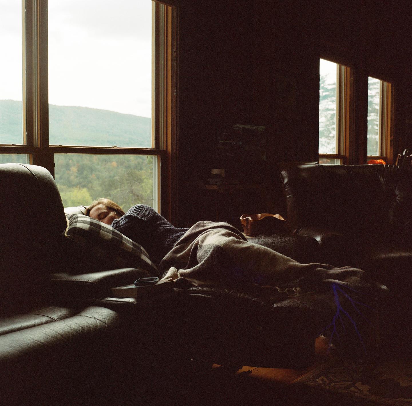 A woman sleeps on a couch next to a window overlooking a mountain.