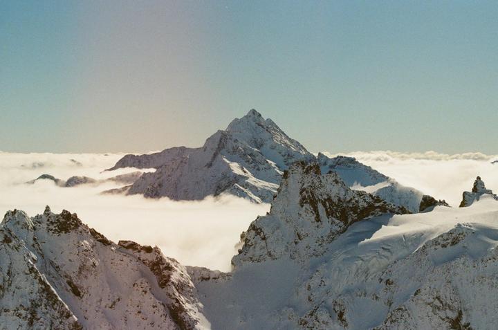 Snow-covered mountains rise above a sea of clouds under a clear sky.