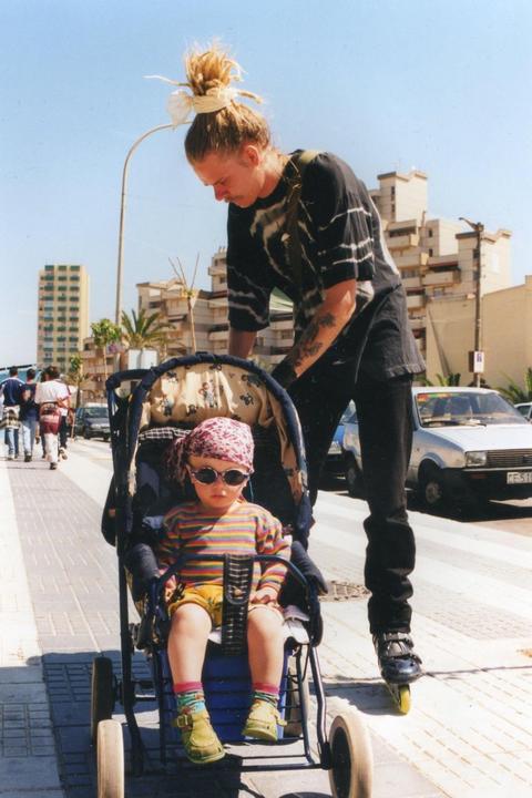 A man on rollerblades pushes a child in a stroller on a sunny street in Gibraltar.