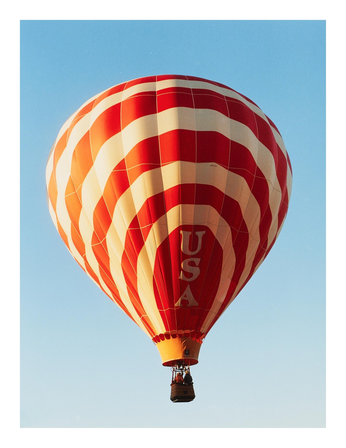 A red and white striped hot air balloon with "USA" written on its side floats in a clear blue sky.