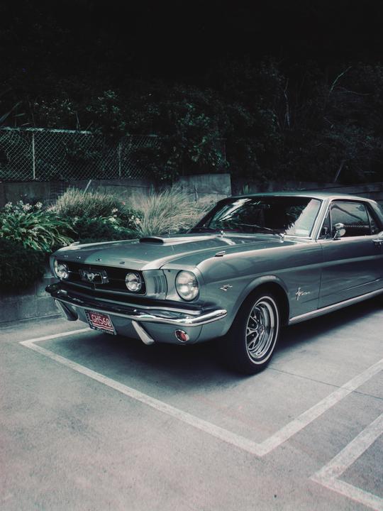 A classic car is parked in a parking space next to a fence and bushes.