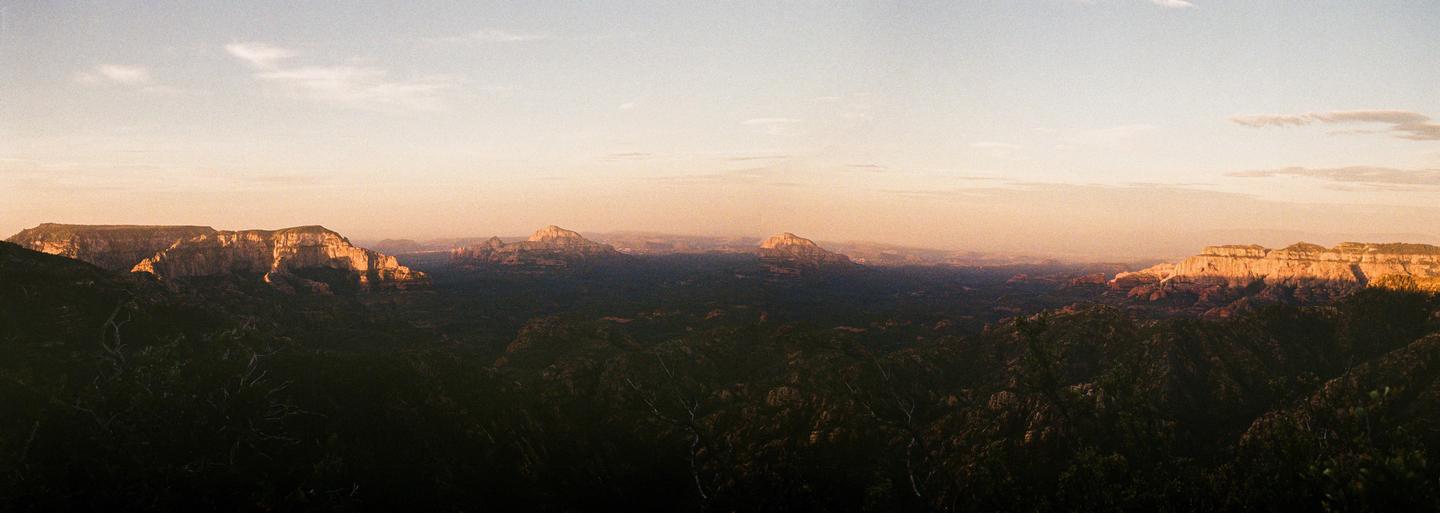 A panoramic landscape shows a valley with mountains in the distance under a hazy sky.