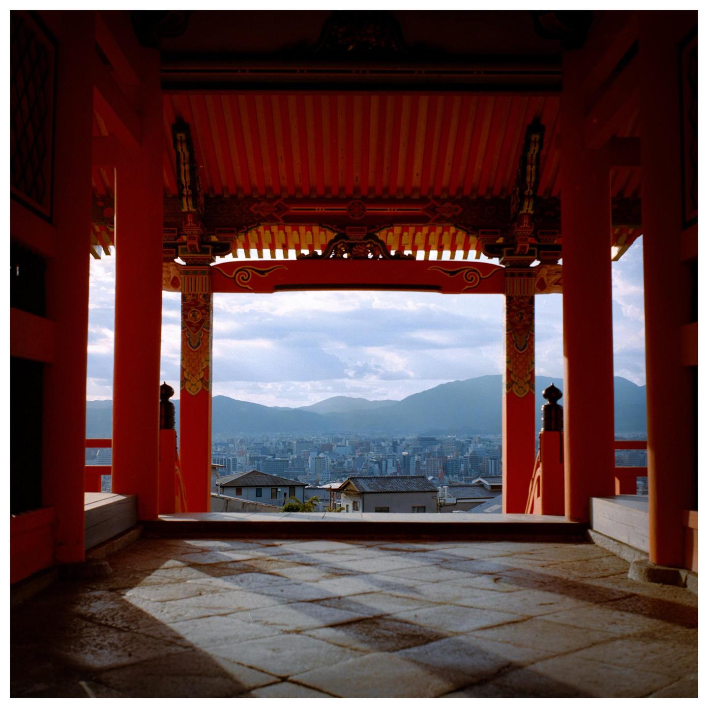 A city with mountains in the background is viewed from a red temple.