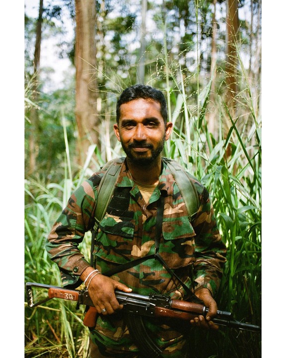 A man in camouflage holds a rifle in a forest.