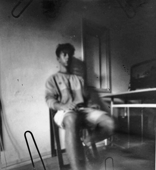 A man sits on a chair next to a table in a blurry, black and white image.