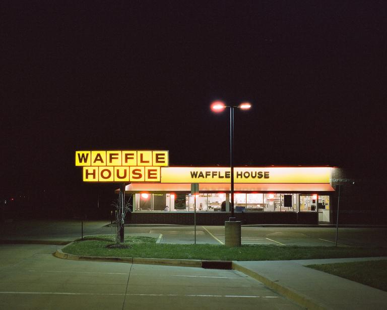A Waffle House restaurant is brightly lit at night, with a street light illuminating the parking lot.