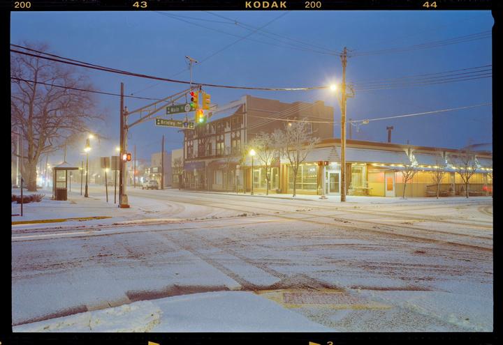 A snow-covered street corner with buildings and streetlights is visible at night.