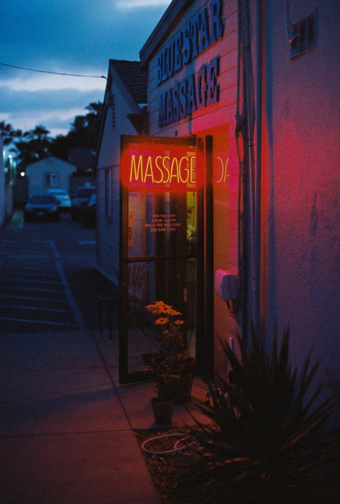 A neon "MASSAGE" sign glows red on the side of a building at dusk.