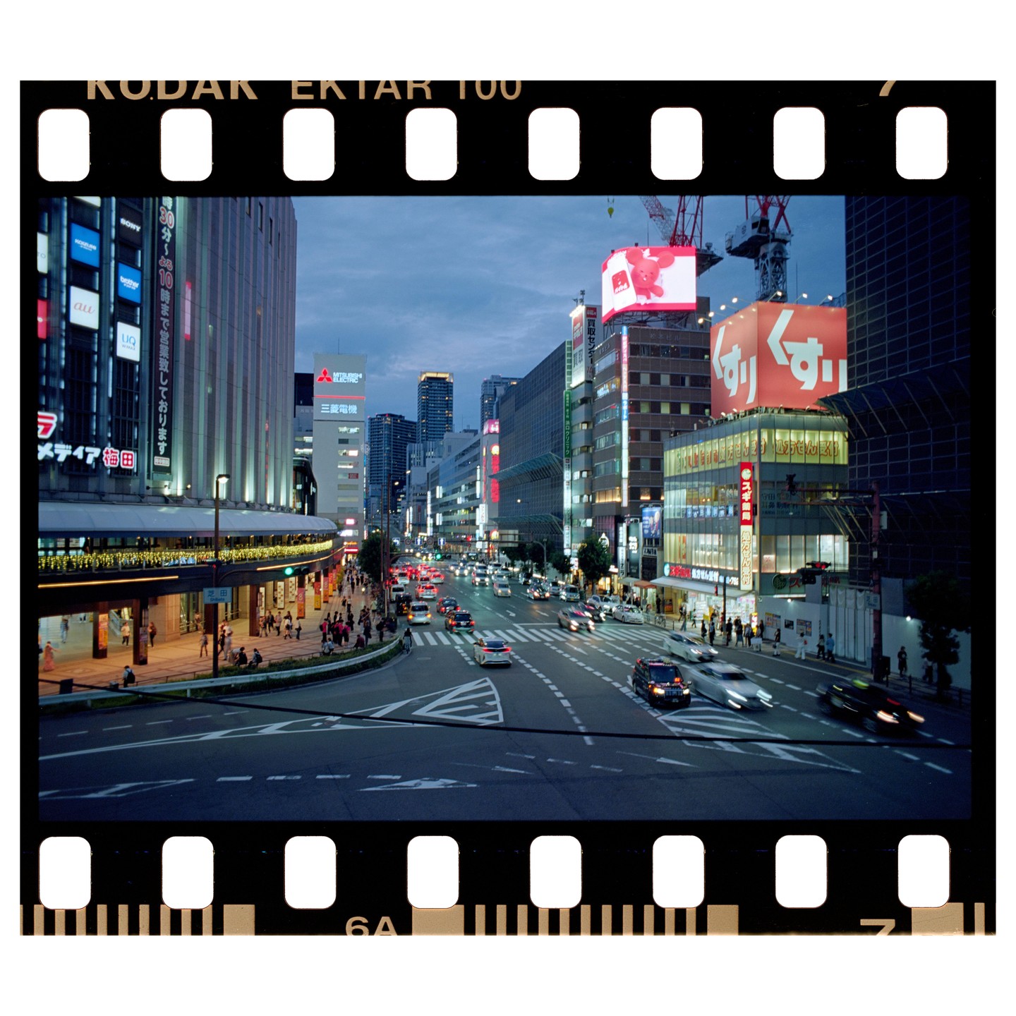 A busy city street at dusk is filled with cars and pedestrians, with tall buildings and bright signs lining the road.
