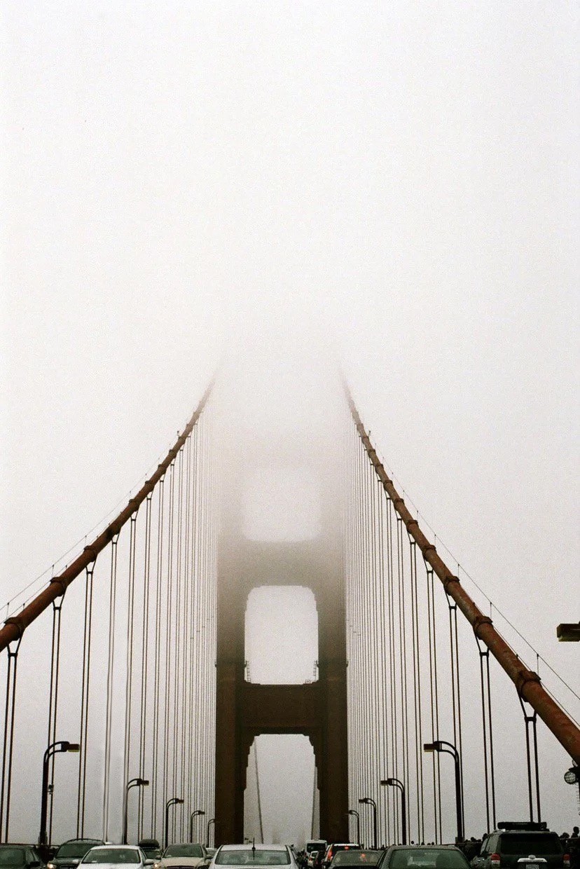 The Golden Gate Bridge is shrouded in fog, with cars visible on the road below.