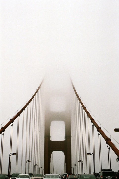 The Golden Gate Bridge is shrouded in fog, with cars visible on the road below.