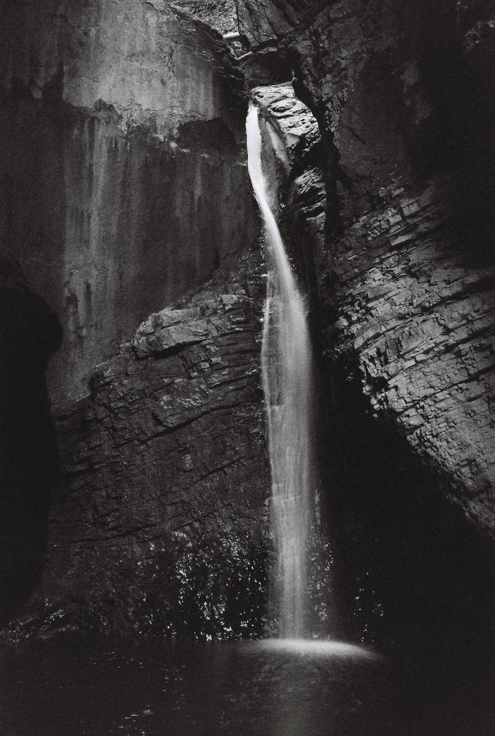 A waterfall cascades into a pool surrounded by dark, rocky cliffs.