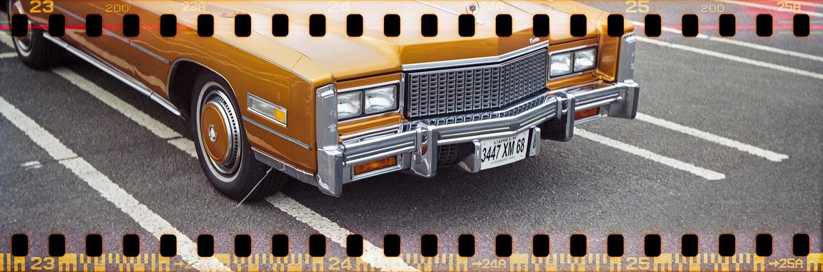 A gold vintage car is parked on asphalt with white lines.