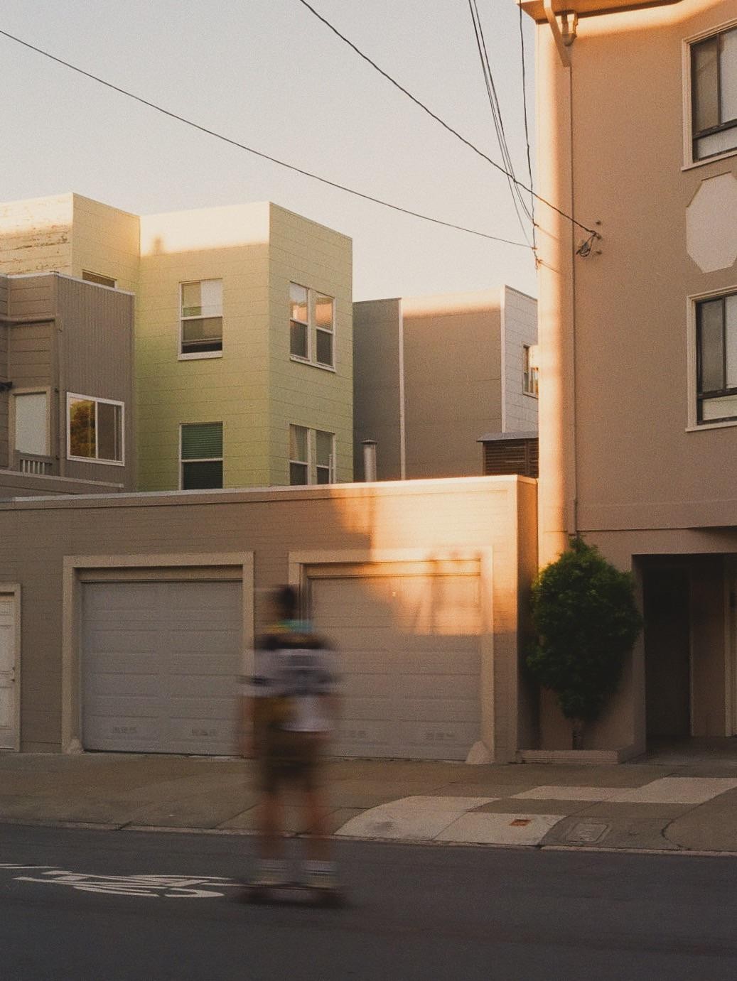A blurry person on a skateboard moves past garages and buildings in the Richmond District of San Francisco.