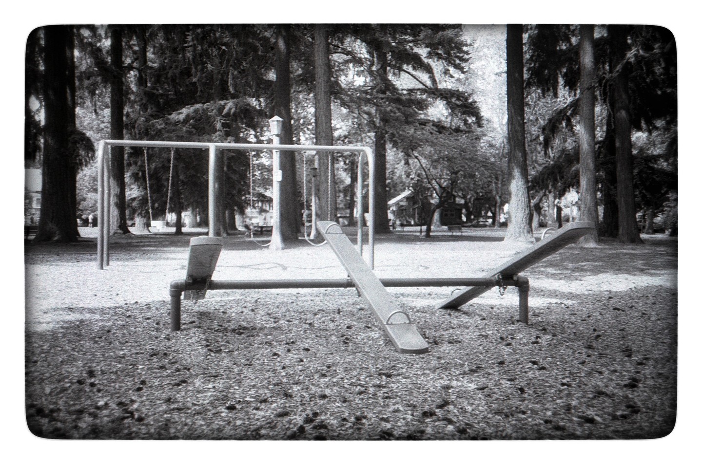 A seesaw and swing set are visible in a park with many trees.