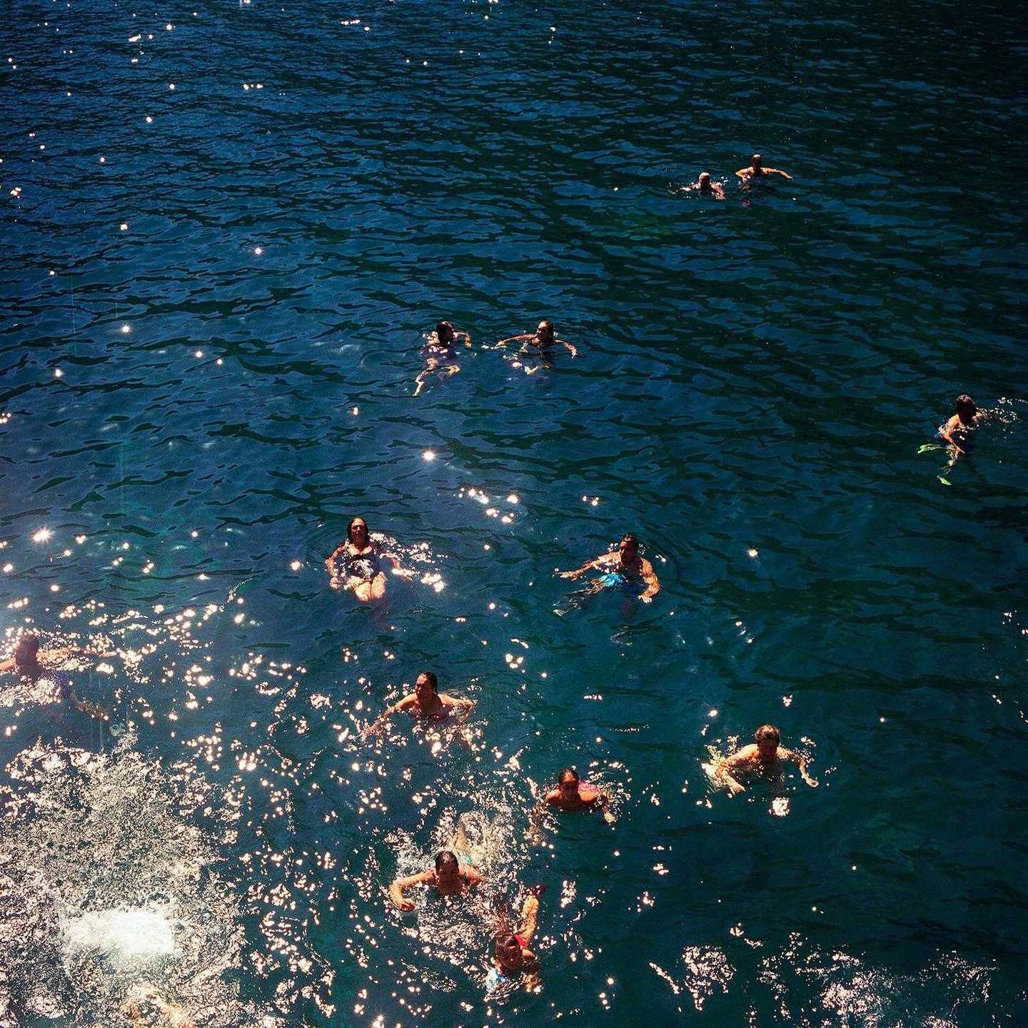 A group of people swim in sparkling blue water.