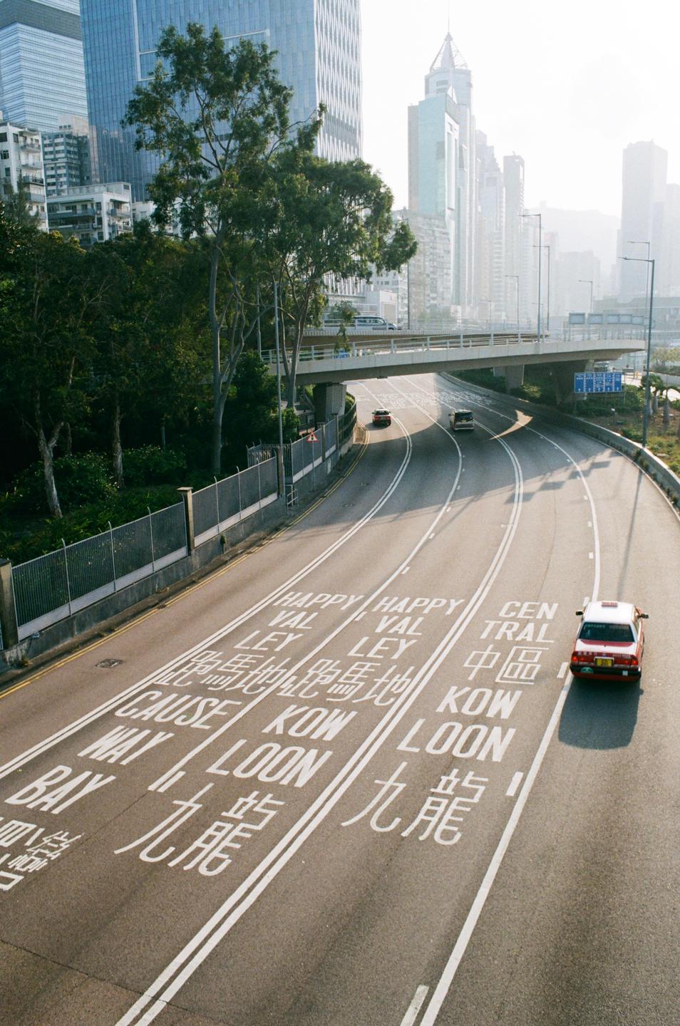A multi-lane highway with cars and an overpass is surrounded by tall buildings and trees.