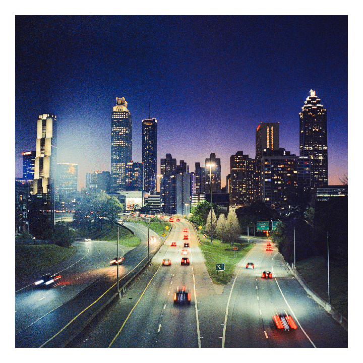 A highway with blurred car lights leads into a city skyline at dusk.